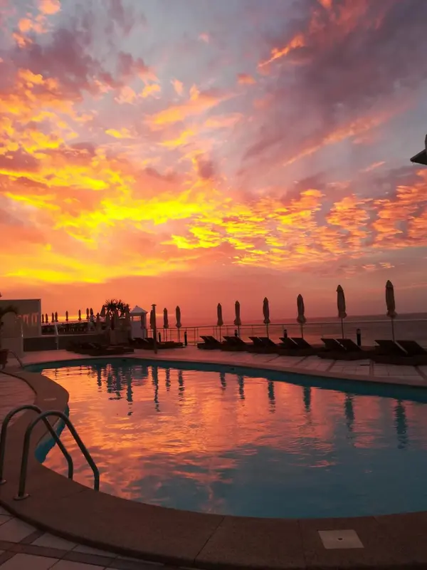 Ciel flamboyant au coucher du soleil sur une piscine et des transats.