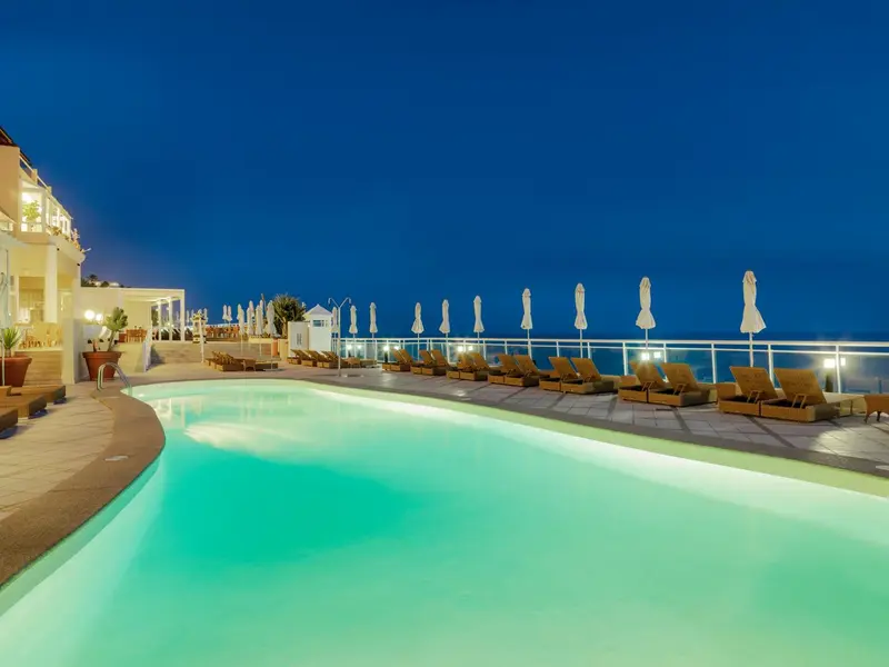 Piscine illuminée avec transats et parasols au bord d'une terrasse.