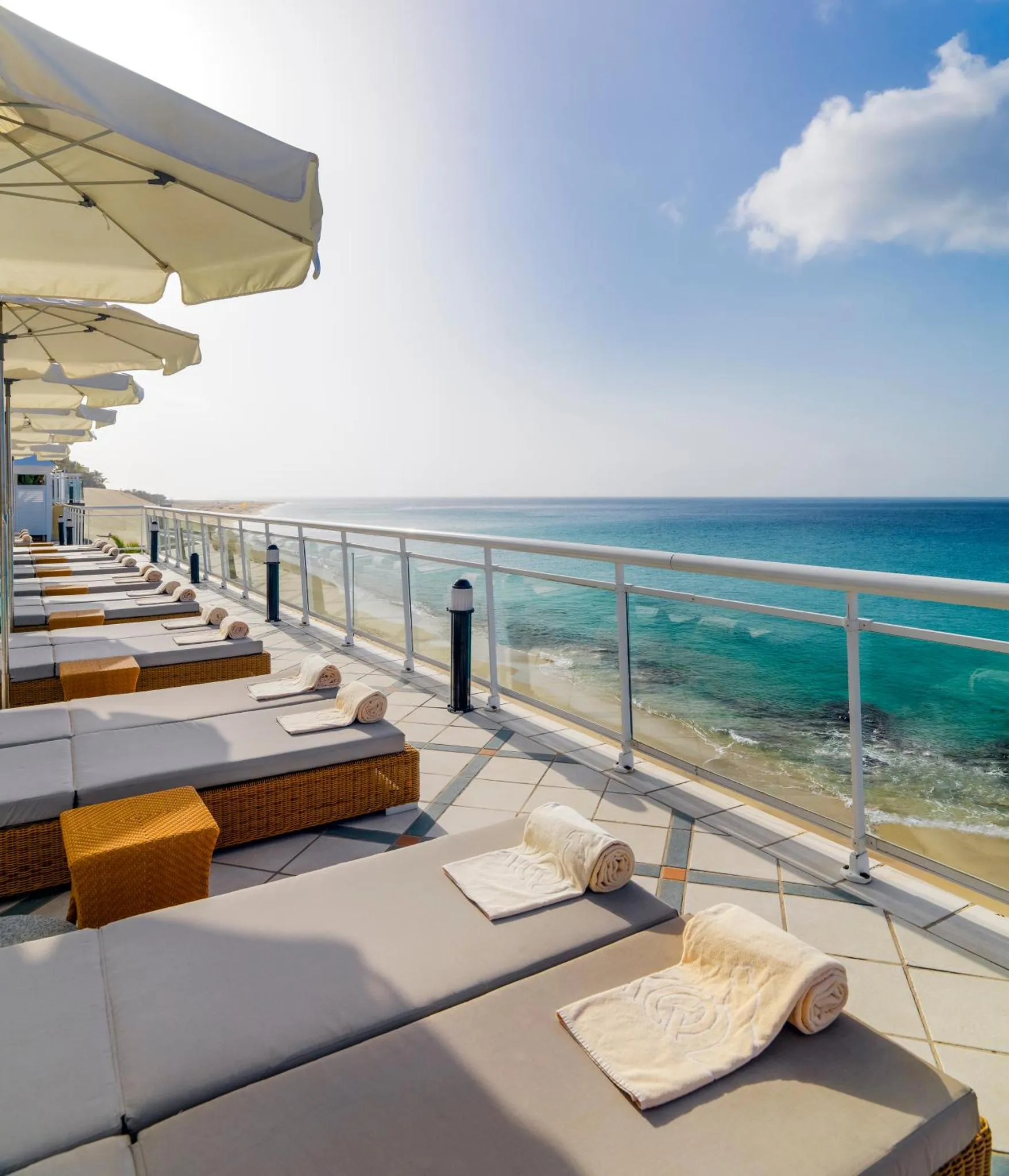 Transats et parasols sur une terrasse ensoleillée avec vue sur la mer.