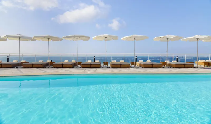 Transats blancs sous des parasols au bord d'une piscine turquoise.