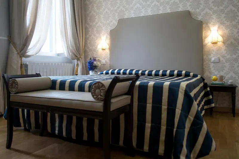 Une chambre avec un grand lit recouvert d'une couette rayée et un banc au pied du lit.