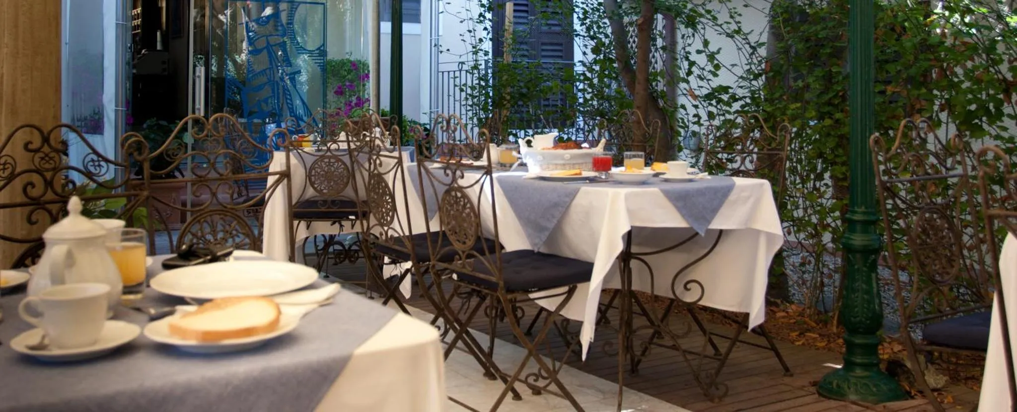 Une table est dressée pour le petit-déjeuner sur une terrasse ombragée.