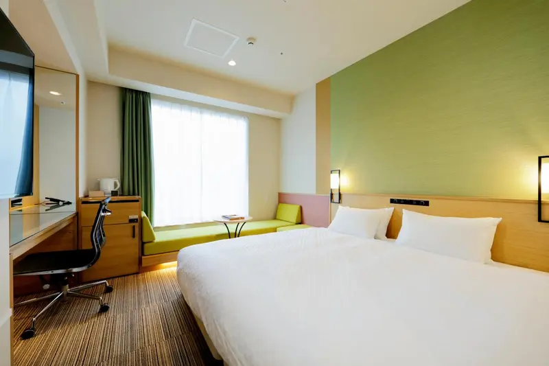 Chambre lumineuse avec un lit blanc et un canapé vert.
