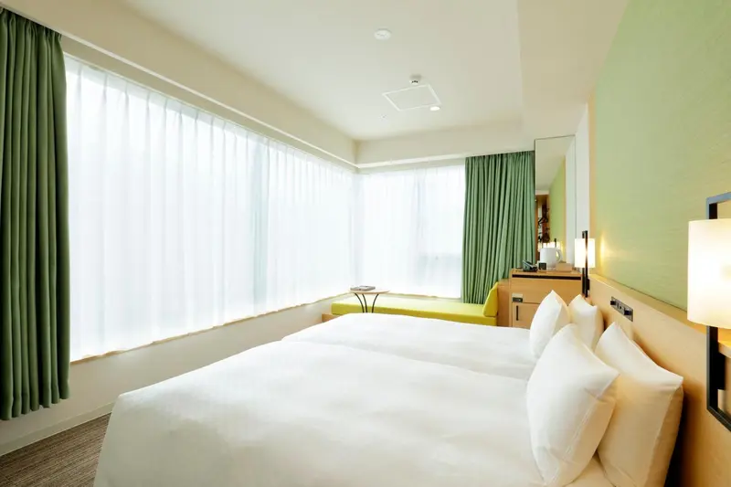 Chambre lumineuse avec un grand lit et un coin lecture près de la fenêtre.