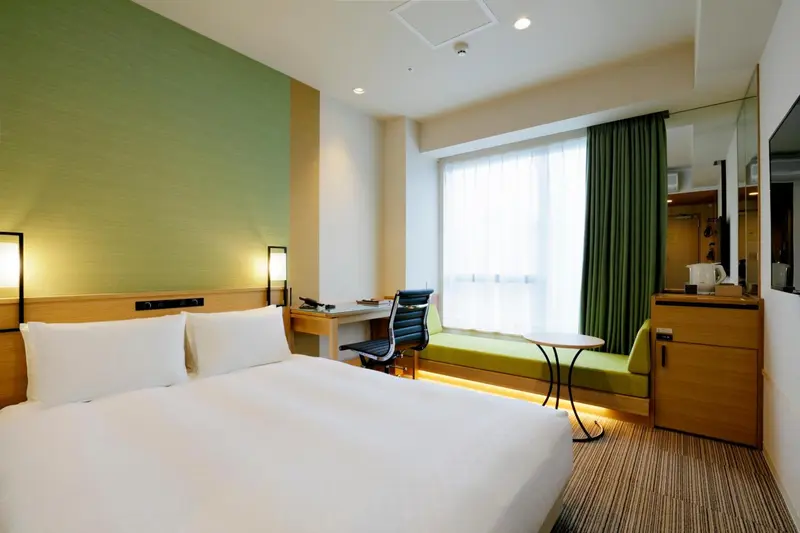 Une chambre d'hôtel lumineuse avec un lit et un bureau près d'une fenêtre.