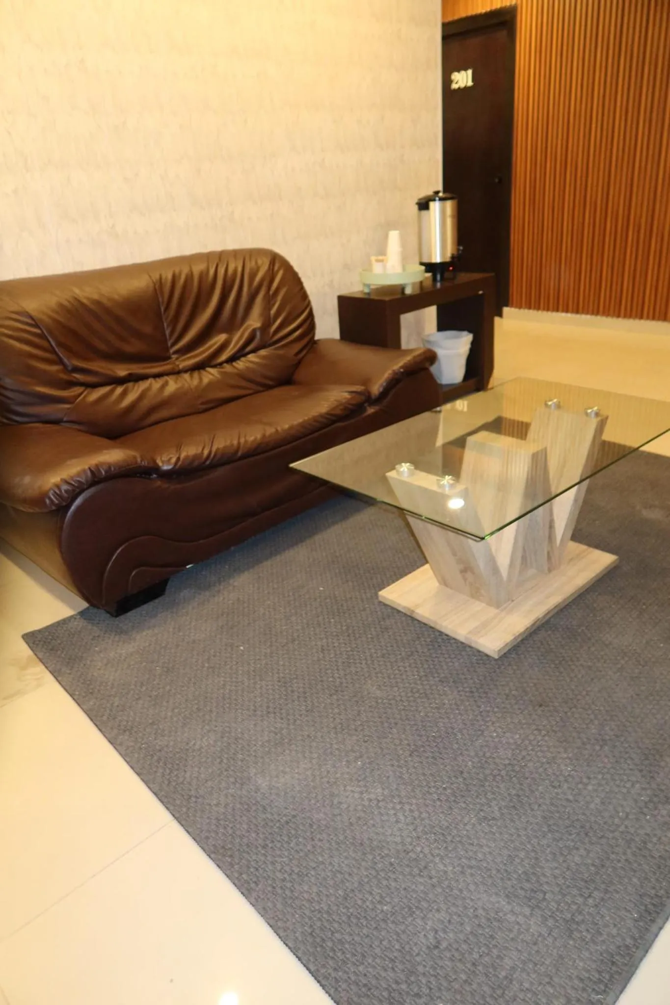 Un canapé en cuir marron et une table basse en verre se trouvent sur un tapis gris.