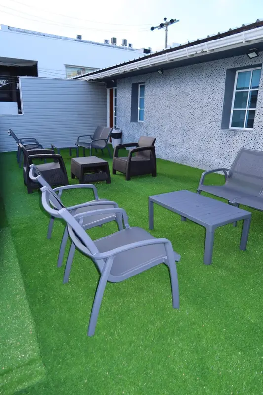Espace extérieur aménagé avec des fauteuils et des tables basses sur une pelouse artificielle.