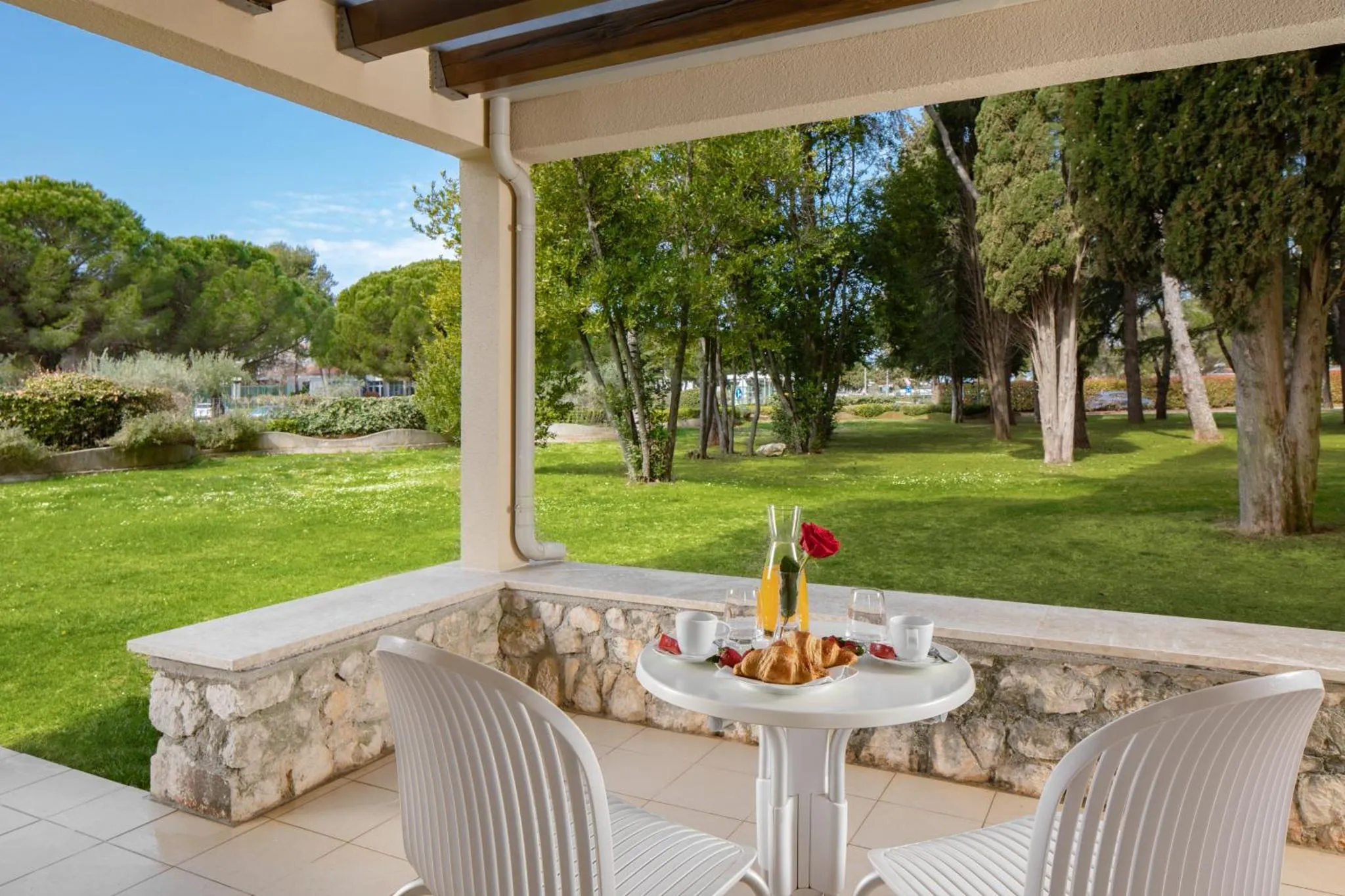 Une table avec des viennoiseries et des boissons est mise en scène sur une terrasse ombragée.
