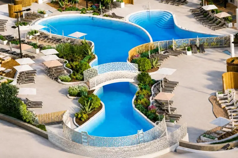 Vue aérienne d'une piscine sinueuse avec des transats et des parasols.