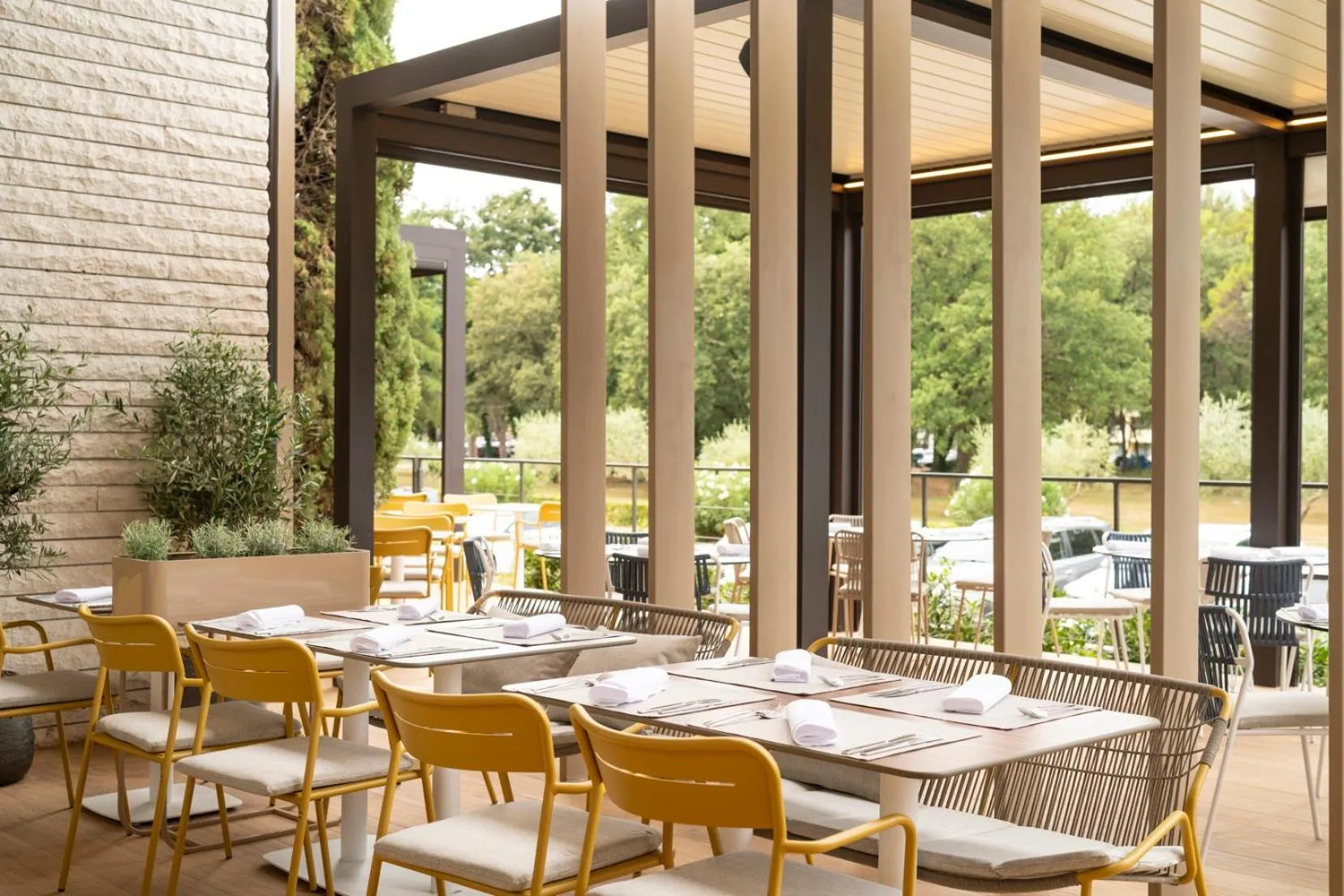 Tables et chaises jaunes disposées sur une terrasse ombragée avec vue sur la végétation.
