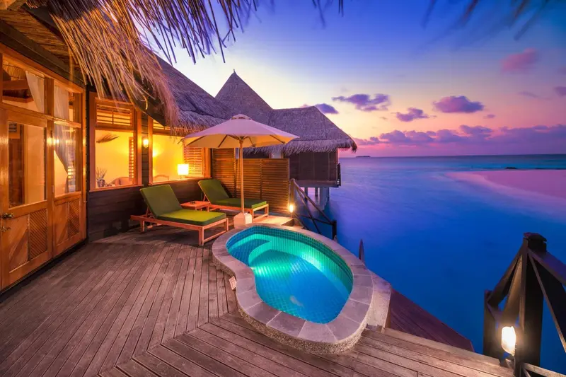 Terrasse en bois avec jacuzzi et mobilier de détente face à l'océan au coucher du soleil.