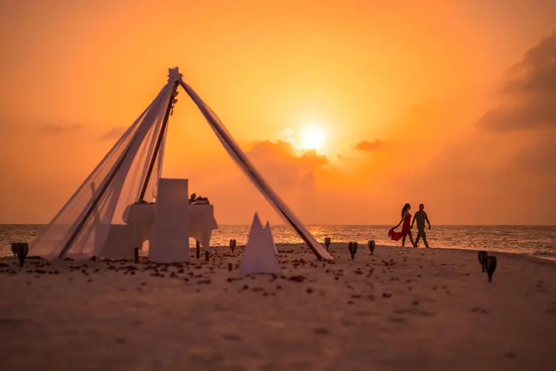 Une plage au coucher du soleil avec une installation pour un dîner romantique.