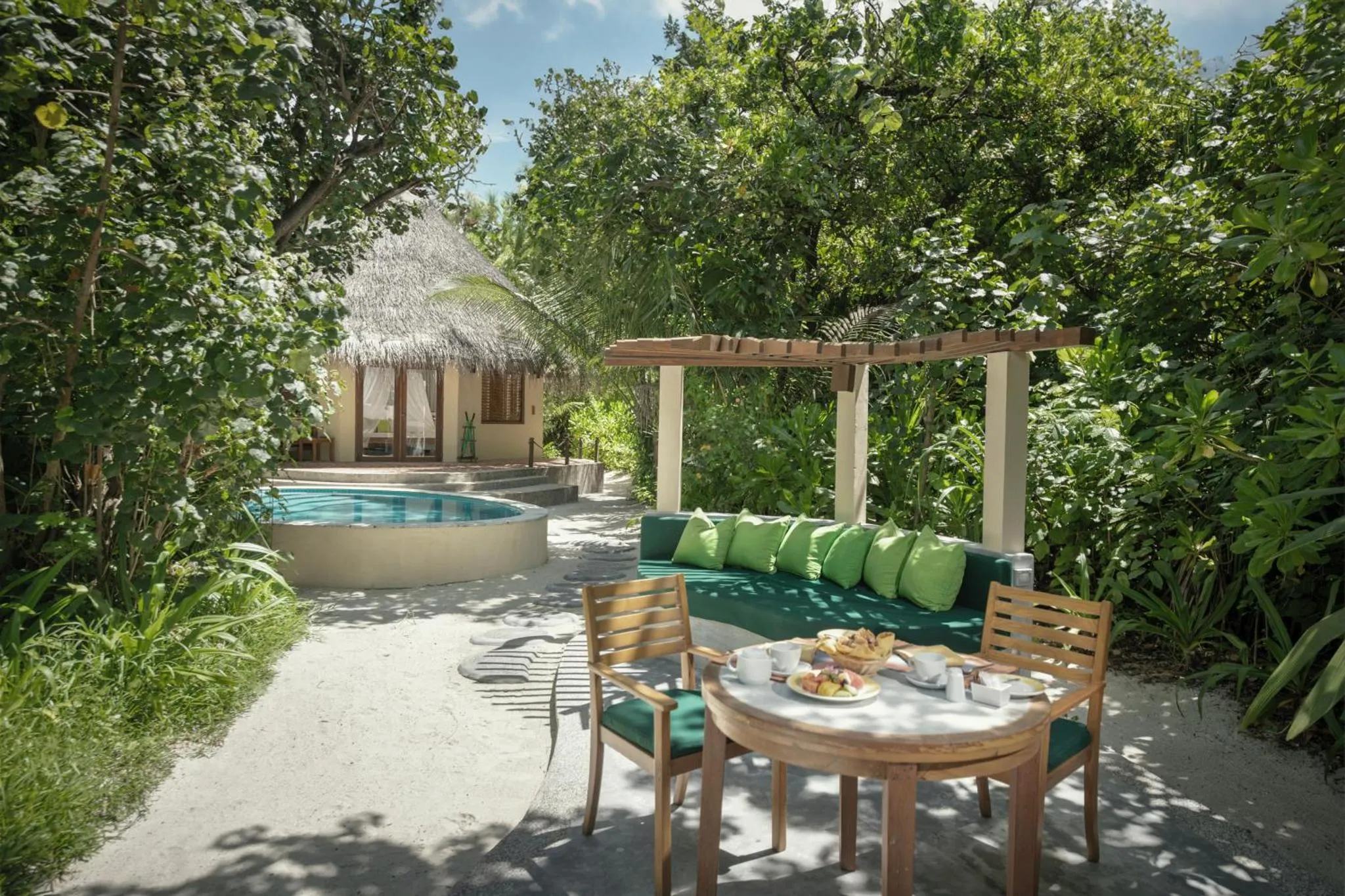 Une terrasse ombragée donne sur une piscine et un bungalow.