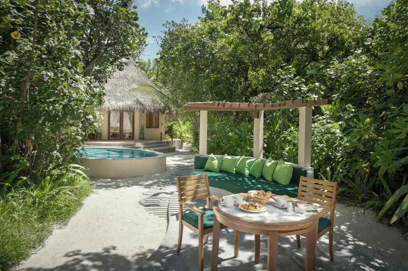 Une terrasse ombragée donne sur une piscine et un bungalow.
