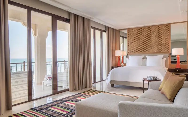 Une chambre lumineuse avec un grand lit et un coin salon donnant sur une terrasse.