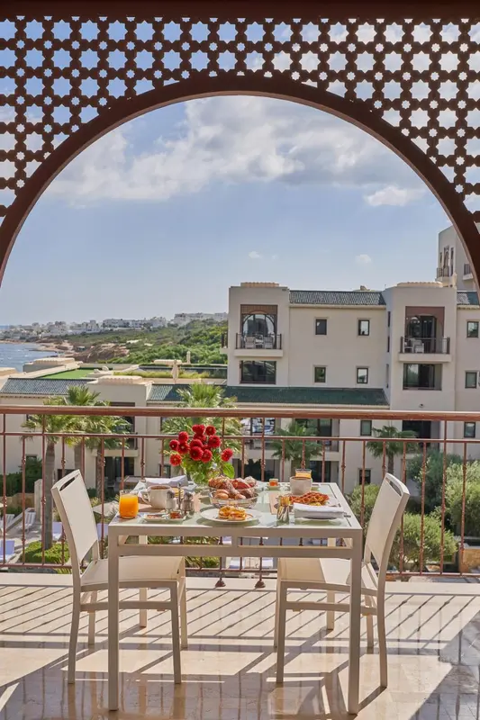 Une table dressée pour un repas en extérieur avec vue sur un bâtiment et la mer.
