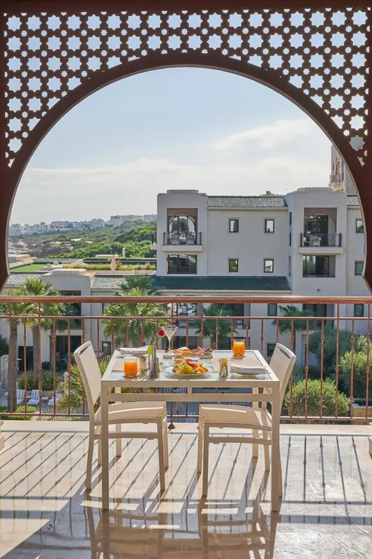 Une table est dressée sur une terrasse avec vue sur un paysage urbain et la mer.