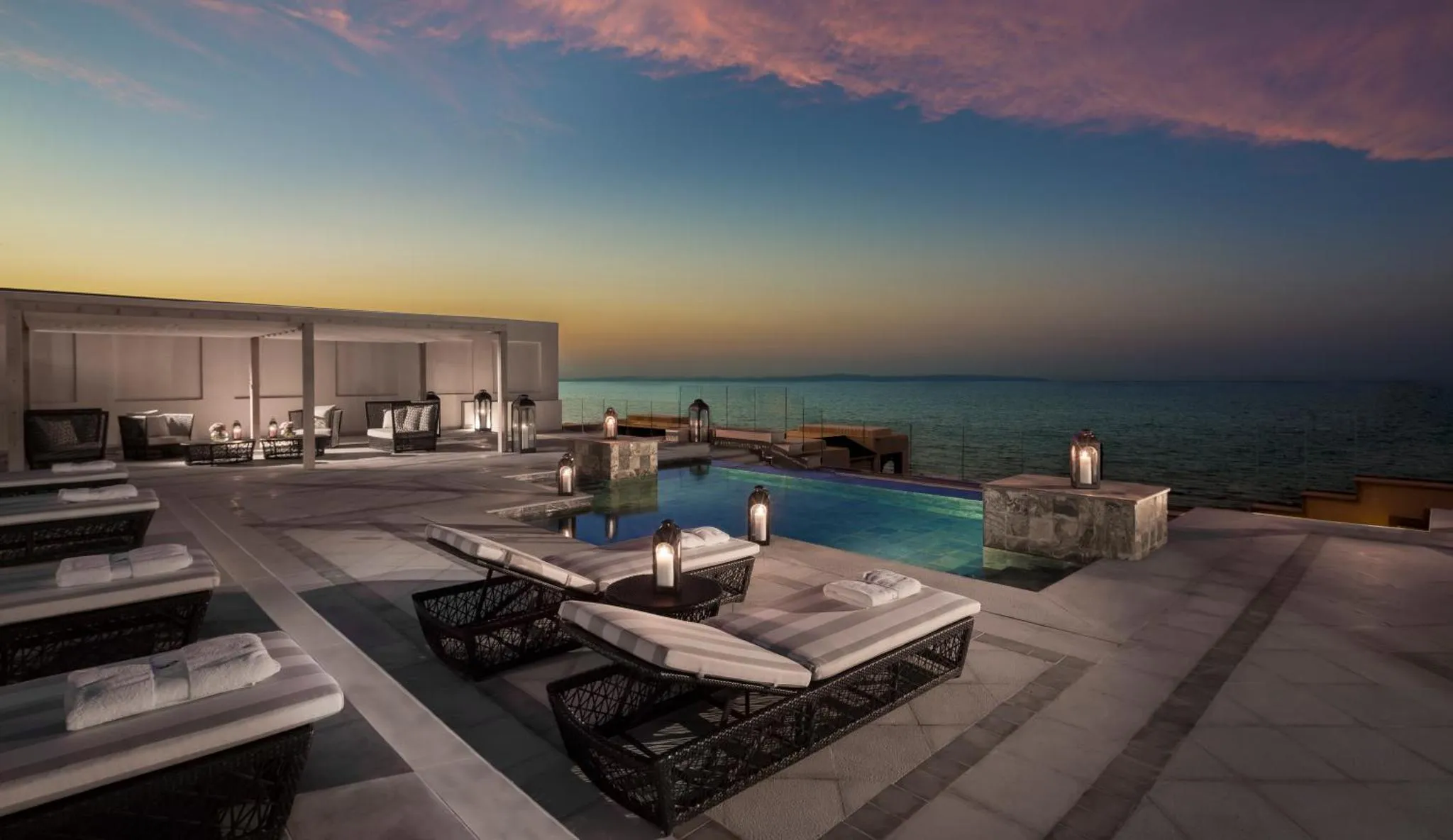 Terrasse avec piscine et vue sur la mer au coucher du soleil.