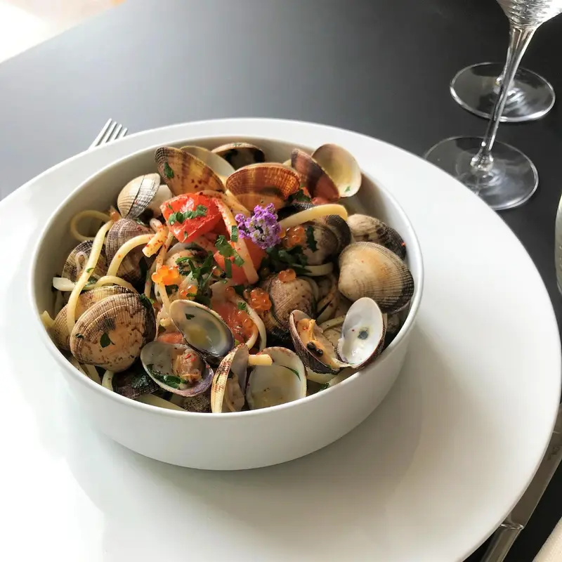 Assiette de pâtes aux fruits de mer, avec un verre de vin en arrière-plan.