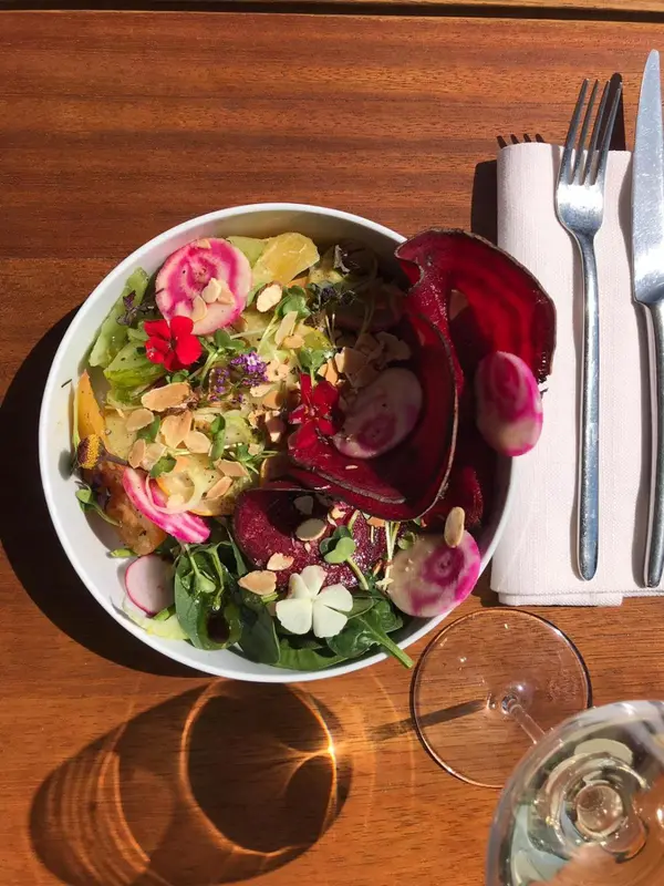 Salade colorée avec des légumes frais et des fleurs comestibles, présentée sur une table en bois.