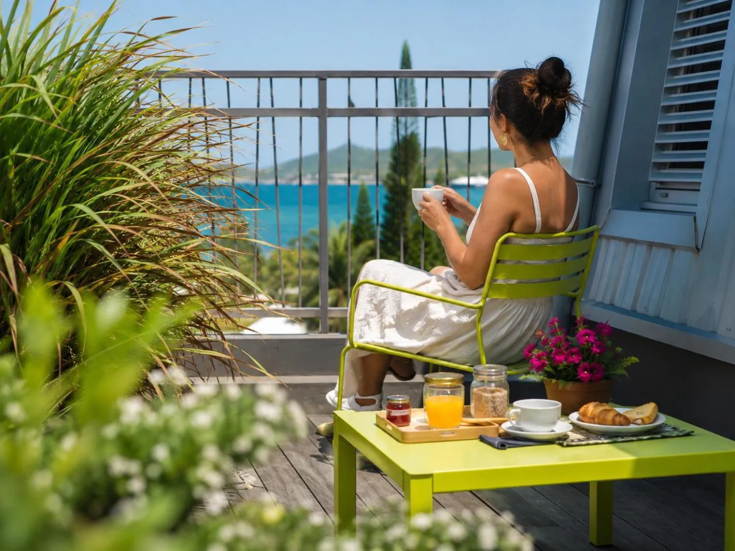 Une femme prend son petit-déjeuner sur une terrasse ensoleillée avec vue sur la mer.