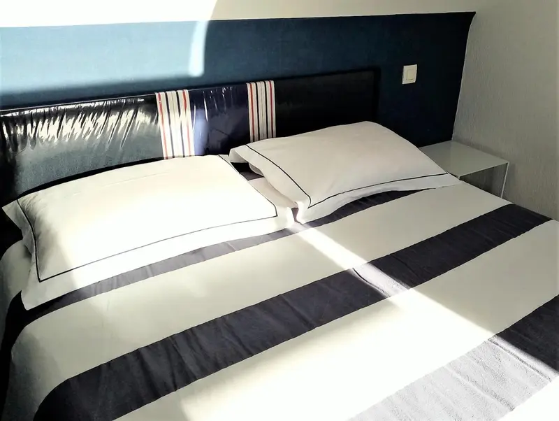 Un lit double avec une couette blanche et des oreillers est prêt dans une chambre.