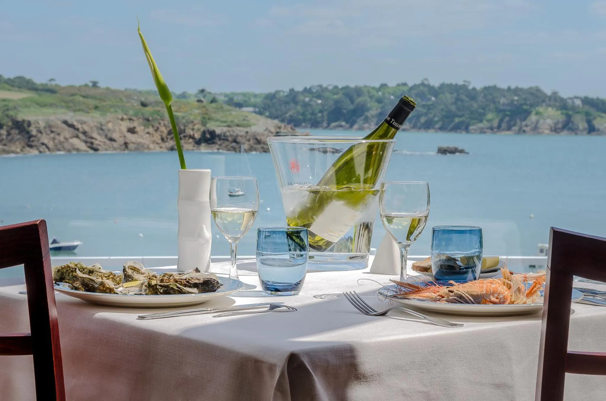 Une table dressée avec des fruits de mer et des boissons offre une vue sur la mer.