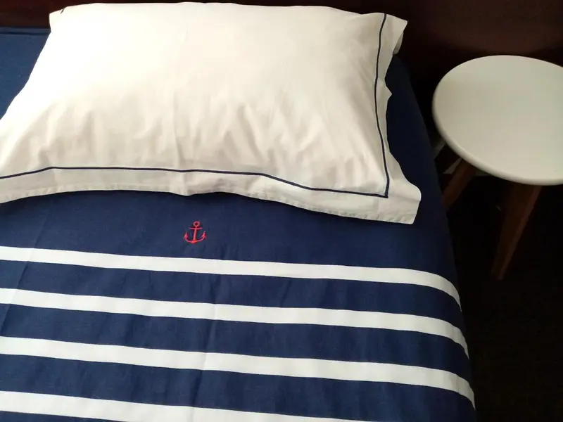 Un lit avec une couette bleu marine et blanche, orné d'une ancre brodée.