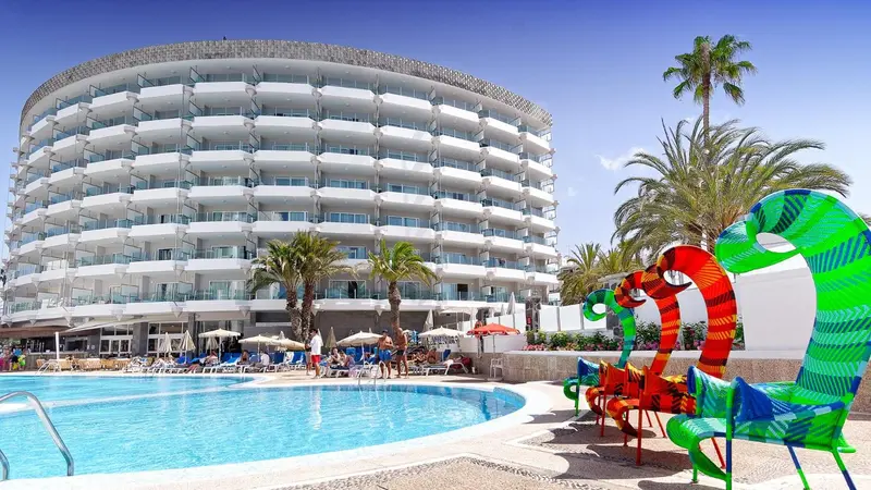 Bâtiment blanc moderne avec des palmiers et une piscine au premier plan.