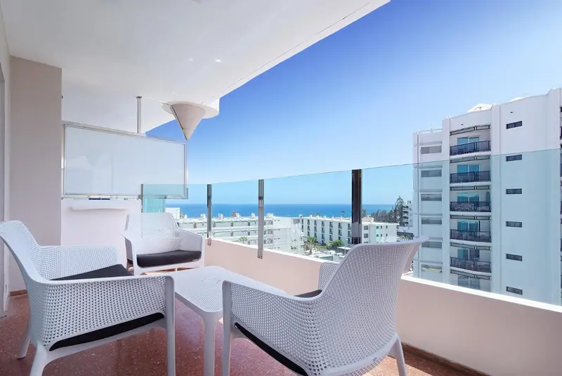 Terrasse aménagée avec mobilier blanc offrant une vue sur la mer et la ville.