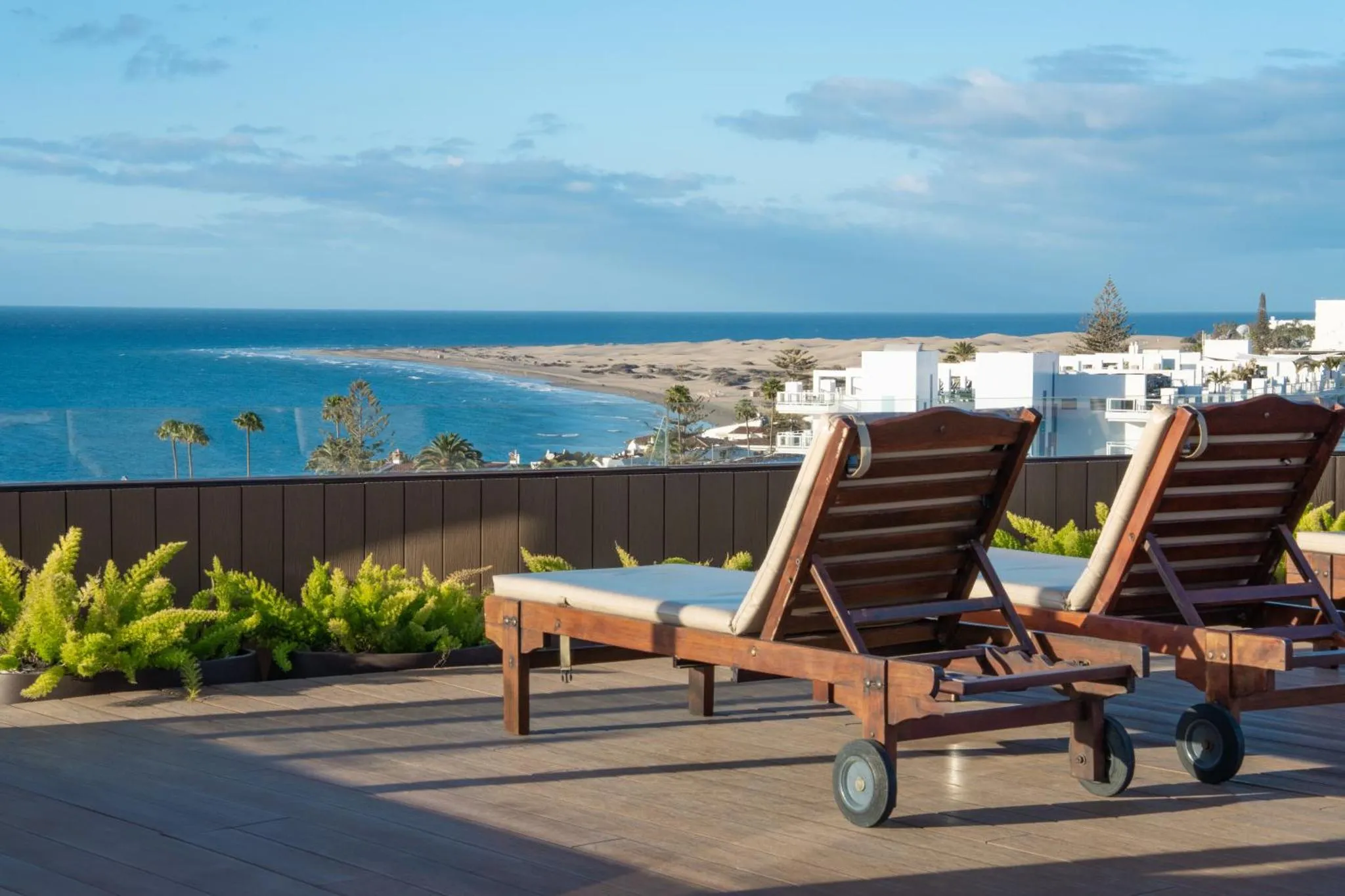 Deux transats en bois sur une terrasse ensoleillée avec vue sur la mer.