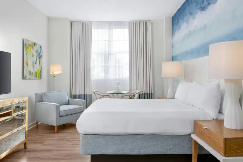 Une chambre lumineuse avec un lit double et un fauteuil.