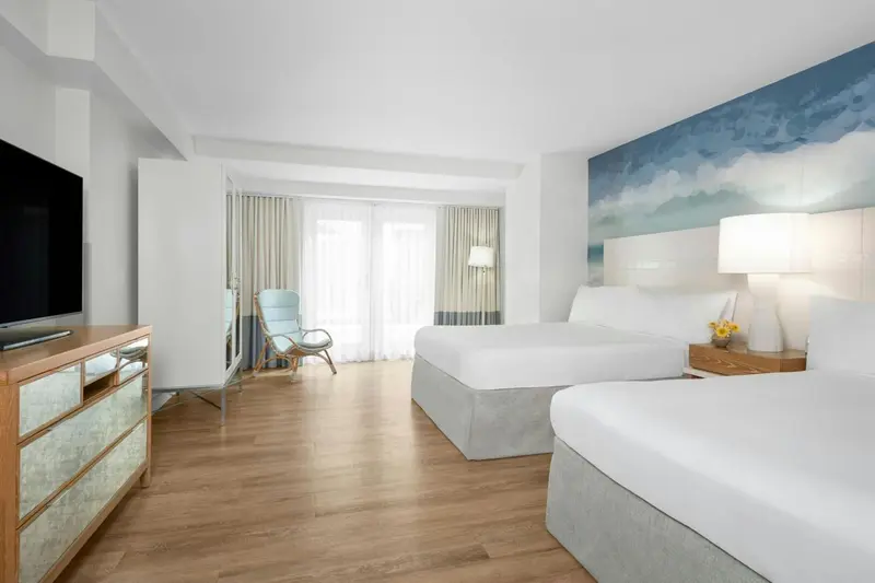 Une chambre lumineuse avec deux lits et un fauteuil près d'une fenêtre.