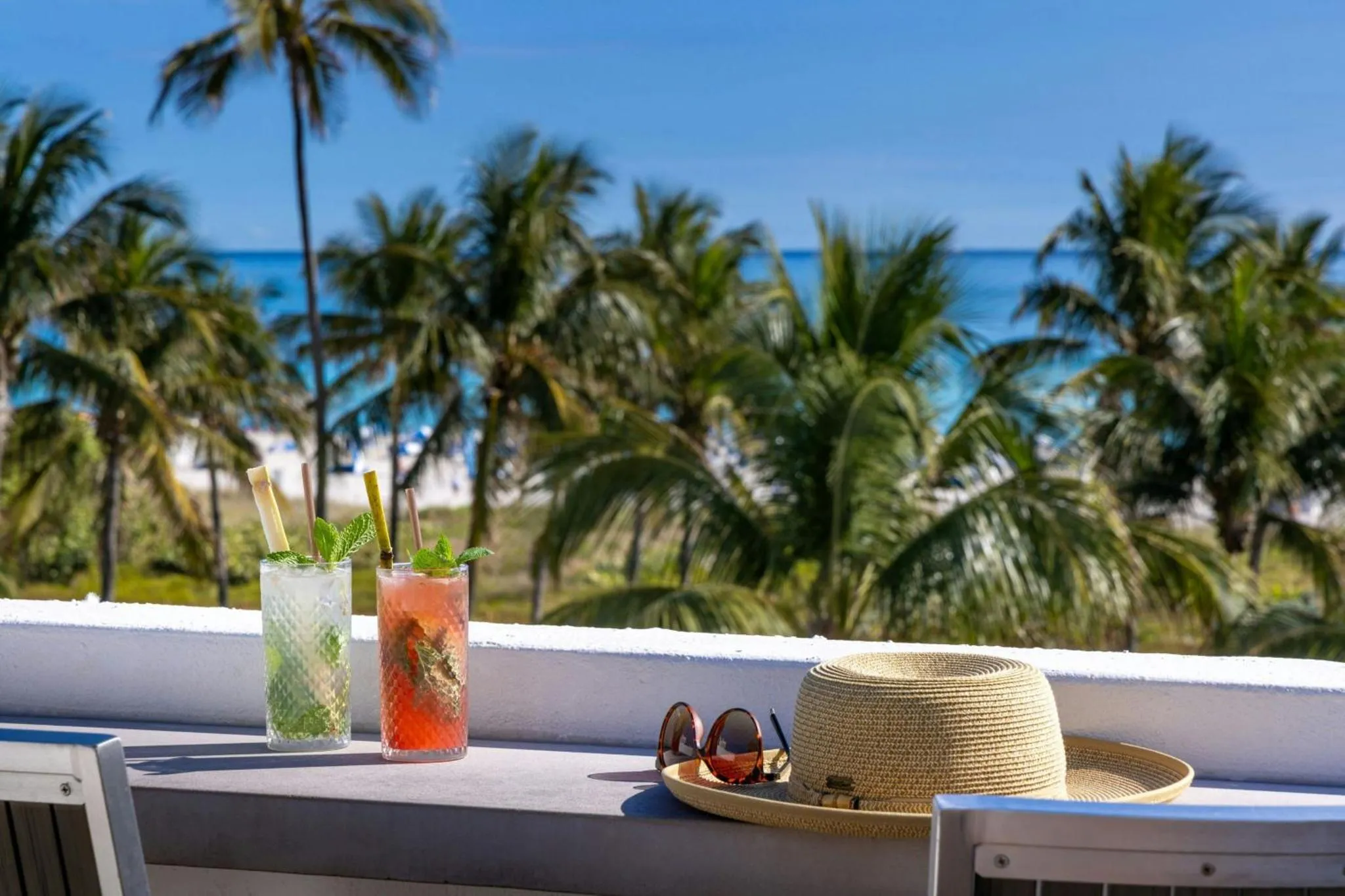 Deux cocktails colorés et un chapeau de paille sur une table en bord de mer.