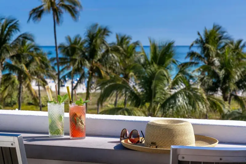 Deux cocktails colorés et un chapeau de paille sur une table en bord de mer.