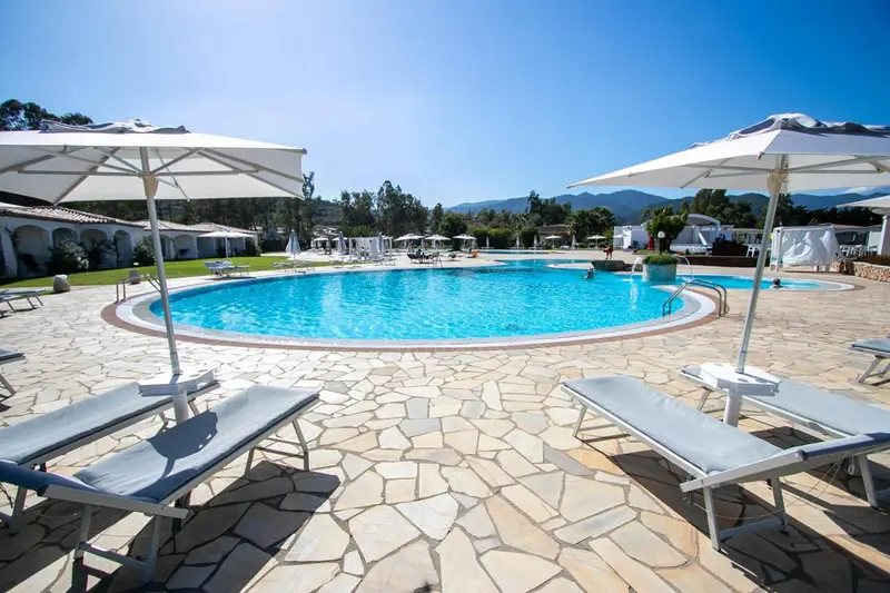 Transats blancs disposés autour d'une piscine rectangulaire ensoleillée.