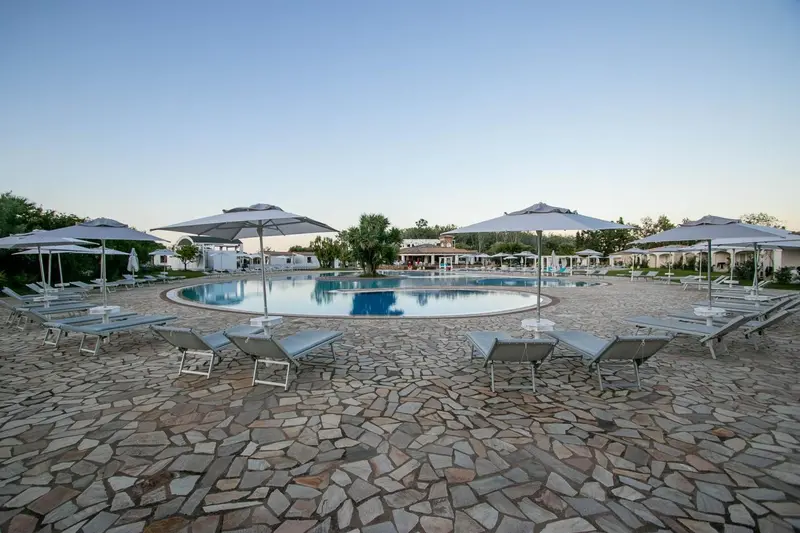 Transats et parasols bordent une piscine de forme ronde dans un espace extérieur pavé.