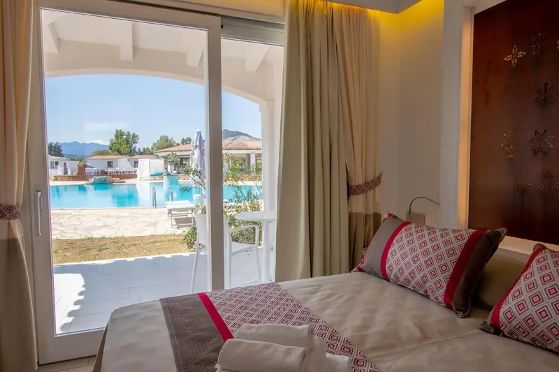 Chambre lumineuse avec un lit et vue sur une piscine ensoleillée.