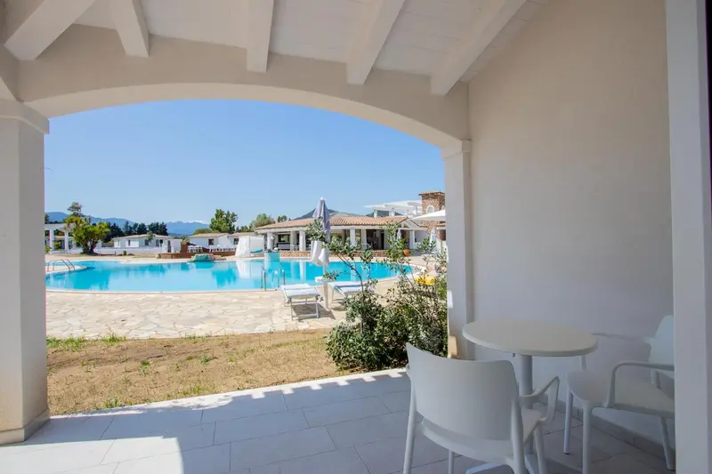 Terrasse ombragée donnant sur une piscine et un paysage verdoyant.