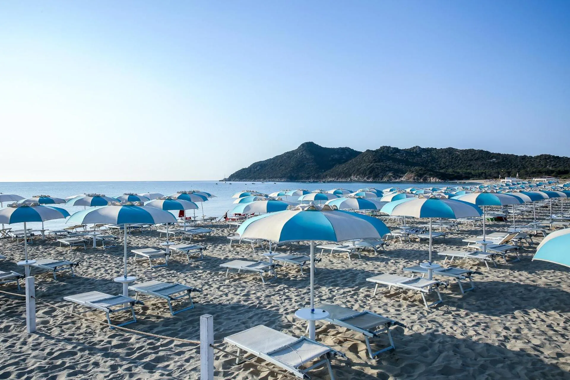 Transats bleus et parasols sur une plage de sable fin face à la mer.