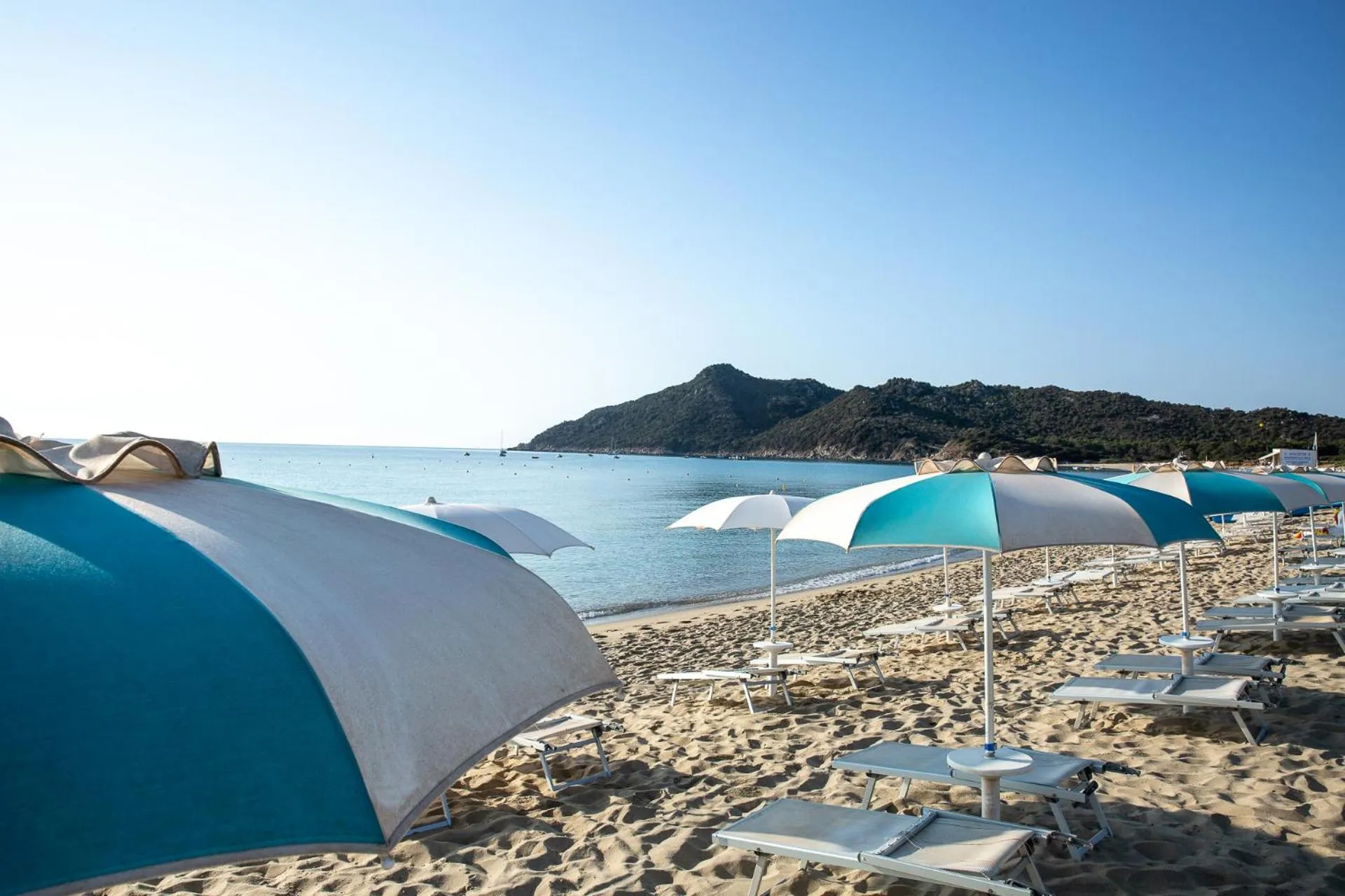 Transats et parasols sur une plage de sable fin face à la mer.