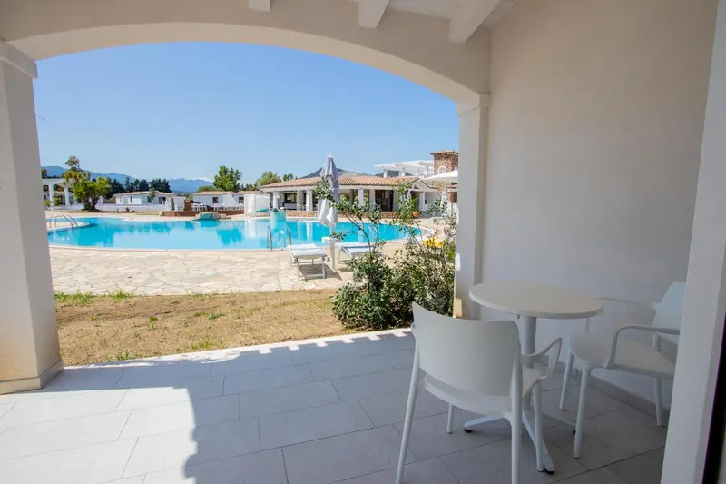 Vue sur une piscine depuis une terrasse ombragée avec table et chaises.