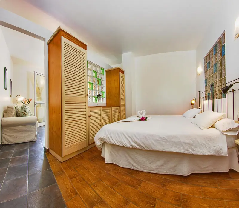 Une chambre lumineuse avec un grand lit recouvert de blanc et un coin salon.