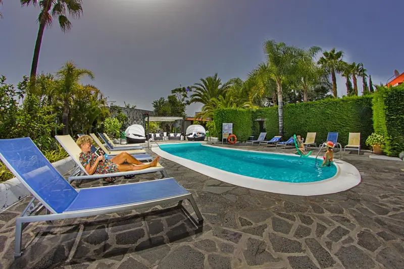 Transats bleus disposés autour d'une piscine rectangulaire dans un jardin tropical.
