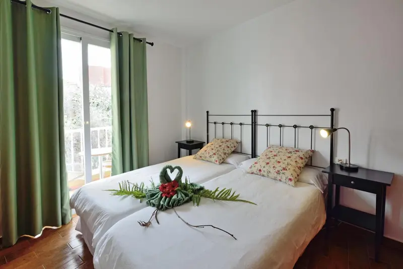 Chambre lumineuse avec un lit à deux personnes décoré de fleurs et d'un balcon.