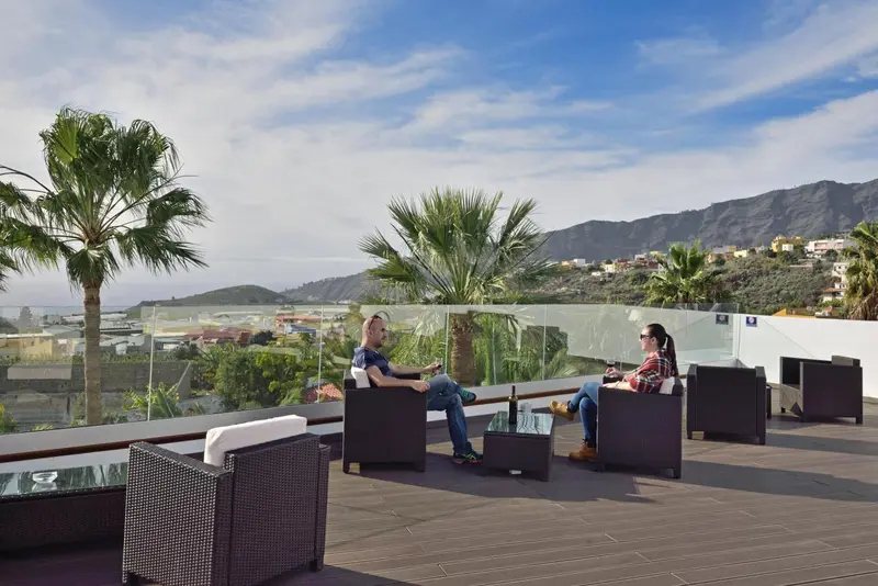 Deux personnes assises sur une terrasse ensoleillée avec vue sur un paysage montagneux.