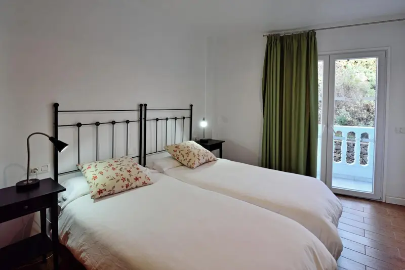 Une chambre lumineuse avec un lit recouvert d'une courtepointe florale et un accès à une terrasse.