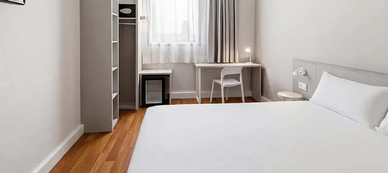 Une chambre lumineuse avec un lit blanc et un bureau.