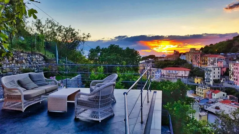 Terrasse aménagée avec canapés et tables basses donnant sur un village côtier au coucher du soleil.