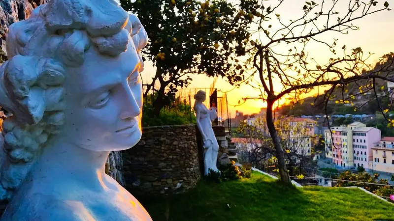 Statue antique en pierre sur une pelouse verdoyante avec vue sur la mer au coucher du soleil.